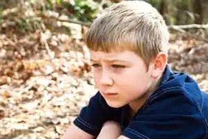 A young boy sitting outdoors, maybe he's thinking, not feeling well, or lost, the expression could relate to many emotions.