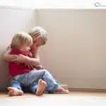 Unhappy Children Sitting On Floor In Corner At Home