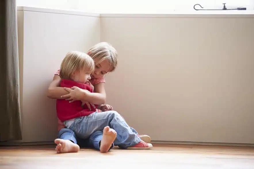 Unhappy Children Sitting On Floor In Corner At Home