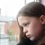 Sad girl looking out of a rainy window