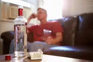 Man Sitting On Sofa With Bottle Of Vodka And Cigarettes