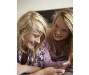 Two Teenage Girls Lying On Bed With Mobile Phone